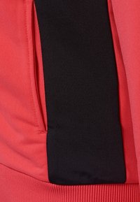 Tissu de sweat-shirt rouge avec un panneau noir contrastant sur le côté. Présente une texture côtelée en bas, mettant en valeur le design sportif.