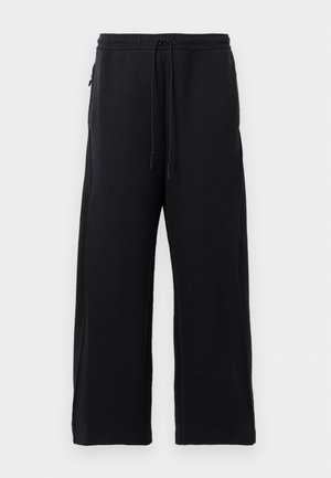 Black sweatpants made of soft fabric, featuring a drawstring waist, wide leg design, and side pockets with a smooth texture.