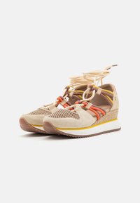 Zapatillas cuña que cuentan con ante beige, paneles de malla y detalles elásticos coloridos, con una suela texturizada; realzadas por una media suela blanca y amarilla.