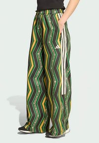 Zaļas, melnas un dzeltenas rakstainas platleņķa bikses ar zīgzaga dizainu, elastīgu jostu un sānu kabatām; ar baltu zīmola aprakstu.