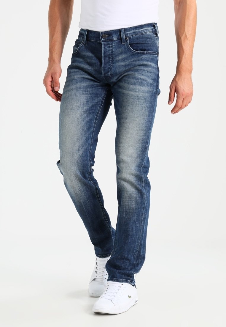 Jeans de denim azul con un corte slim, acabado desgastado y detalles de costura. Presenta cinco bolsillos y una cremallera con un botón de metal.