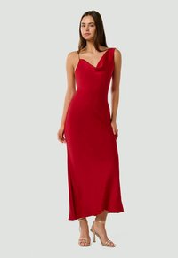 Rochie roșie cu un design cu un singur umăr, realizată dintr-un material neted care se așază până la jumătatea gambei. Prezintă un decolteu discret în formă de cowl și o siluetă elegantă.