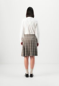 Weißes Langarmhemd kombiniert mit einem gefalteten grauen Karorock. Schwarze Schuhe und beige Socken runden das Outfit ab. Einfaches, funktionales Design.