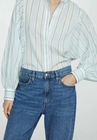 Gestreepte button-up blouse in lichtblauw, wit en groen, met een relaxte pasvorm en pofmouwen, gecombineerd met hooggelegen blauwe jeans.