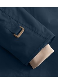 Die Ärmel der navyblauen, wasserdichten Jacke sind mit einem tanfarbigen, gerippten Baumwollbund und einem goldenen Metallverschluss verziert. Glattes, strapazierfähiges Material mit detaillierter Nahtführung.