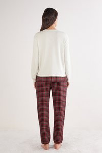 Top de manga larga crema combinado con pantalones de pijama de cuadros rojos que presentan acentos en negro y verde. Textura suave, ajuste relajado. Sin herrajes visibles.