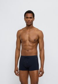 Μπλε σκούρα ανδρικά μαγιό κατασκευασμένα από ελαστικό ύφασμα, με ελαστική μέση με κορδόνι, εφαρμοστή  σχεδίαση και μικρό λογότυπο στο πλάι.