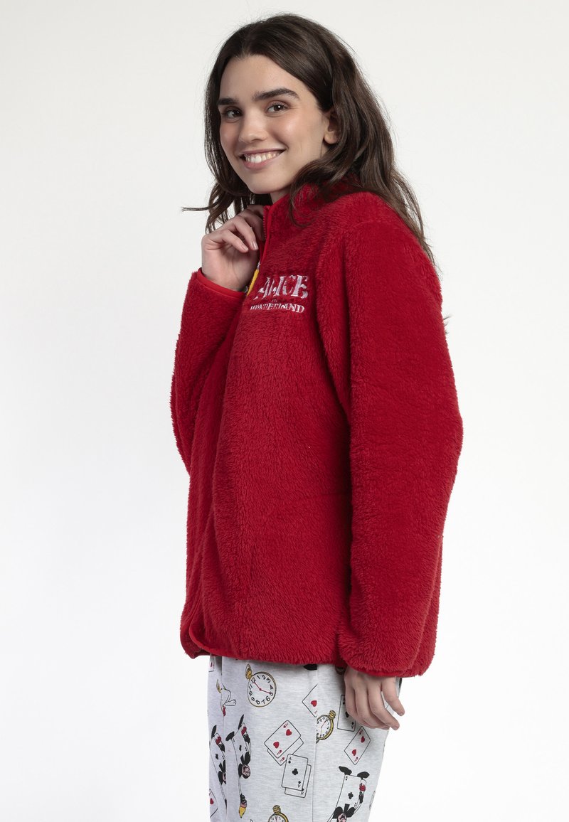 Pulóver de forro polar rojo con un cuello alto, que presenta un estampado gráfico en el pecho. Combinado con pantalones de pijama grises estampados. Textura suave.