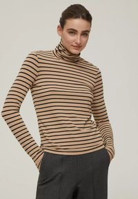 Maglione a collo alto a righe beige con righe orizzontali nere; tessuto morbido; vestibilità slim; maniche lunghe; infilato in pantaloni grigio scuro.