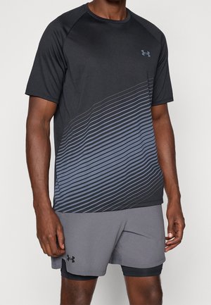Atletisk person iført en sort og grå Under Armour kortærmet skjorte med diagonale striber og matchende grå shorts med logo.