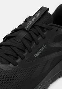 Čierna športová obuv s textilným zvrškom, s textúrovanými akcentmi a šnúrkami. Obsahuje značku Reebok a gumovú podrážku so vzorom pre lepšiu priľnavosť.