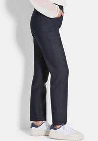 Dunkelblaue Jeanshose mit geradem Bein, Vorder- und Gesäßtaschen sowie glatter Textur, kombiniert mit weißen Sneakers.