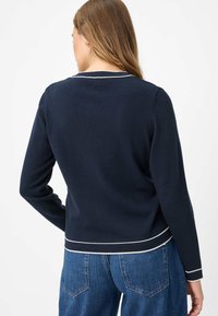 Marineblauer Pullover mit langen Ärmeln, einem runden Ausschnitt und weißem Besatz entlang von Kragen und Saum. Das Material wirkt weich und glatt.