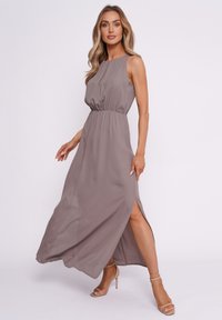 Maxikleid aus hellbraunem Stoff mit elastischem Bund, ärmellosem Design, seitlichen Schlitzen und einer fließenden Silhouette.