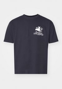 Dunkelblaue Baumwoll-T-Shirt mit kurzen Ärmeln, ausgestattet mit einem weißen grafischen Druck eines Hundes und dem Text „EINHEIMISCHE DIENSTLEISTUNGEN“ auf der Vorderseite.