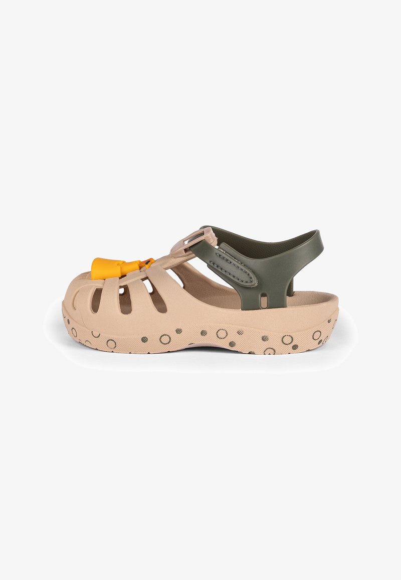 Beige sandal with open-toe design, featuring a green strap and yellow decorative hardware. Textured sole with circular patterns.