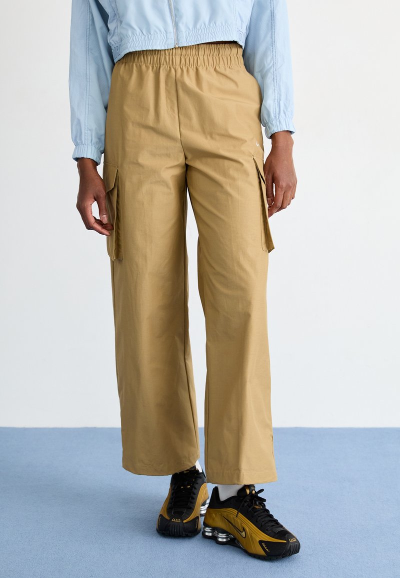 Pantaloni cargo beige a gamba larga con vita elastica, dotati di tasche laterali e una texture liscia, abbinati a scarpe sportive nere.