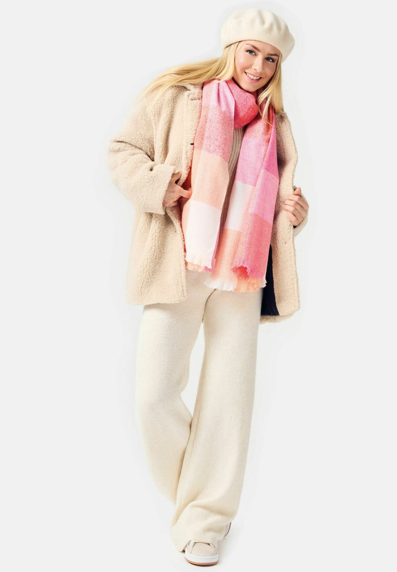 Beige fleece coat, light beige wide-leg pants, and a pink patterned scarf with fringed edges. White beret and light shoes complete the look.