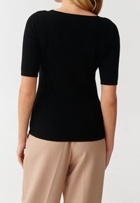 Top corto a maniche corte nero con scollo ampio, design aderente e tessuto testurizzato; indossato con pantaloni beige chiaro.