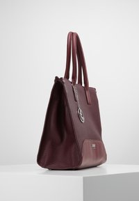 Burgundowa torba typu tote o ziarnistej fakturze, gładkich akcentach, dwóch solidnych uchwytach, zapięciu na zamek i srebrnym zawieszce.