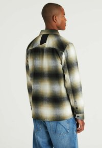 Camicia a quadri nei toni beige, nero e bianco; presenta un dettaglio a scollatura posteriore. Realizzata in tessuto strutturato con polsini a bottoni.