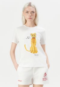 Hvit t-skjorte med leopardgrafikk og teksten "BAD VIBES," sammen med hvite shorts med en rød brodert logo og "REPLAY."