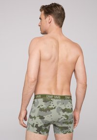 Men's boxer shorts in a green camouflage pattern, featuring a soft elastic waistband with "CAMP DAVID" logo. Short length, stretchy material.
