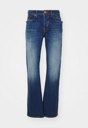 Blaue Jeans mit ausgestelltem Bein, fünf Taschen und einem Messingknopfverschluss. Merkmale sind leichte Ausbleichungen und Kontrastnähte.