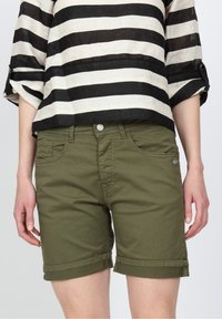 Olivgröna rullade shorts med frontfickor och bälteshällor, kombinerade med en svart och vit randig topp i lös passform. Tygblandning av bomull.