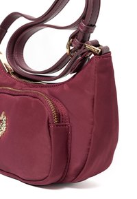 Bordowa torebka z gładkim nylonowym wykończeniem, złotym zamkiem błyskawicznym i podwójnymi ramiączkami. Posiada przednią kieszeń oraz subtelne detale z logo.