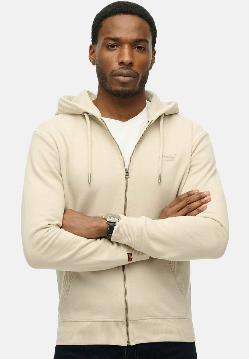 Hoodie beige con zip, cappuccio regolabile con lacci, tasche frontali, polsini a costine e un piccolo logo sul petto. Realizzato in misto cotone.