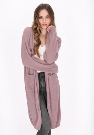 Langer, offen gestalteter Cardigan aus weichem, gestricktem Lavendelmaterial. Er verfügt über zwei vordere Taschen und gerippte Bündchen, kombiniert mit einem schlichten weißen Oberteil und dunklen Jeans.