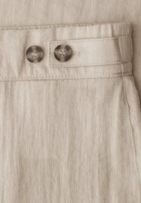 Pantalon en lin beige clair avec deux boutons ronds foncés sur une bande en tissu à la taille et des détails de couture visibles.