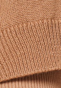 Gros plan sur un tissu tricoté couleur chameau montrant des motifs en côtes et en jersey.