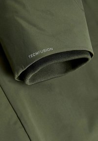 Olive green jacket featuring a textured, fitted cuff with a mesh lining and the brand "TECHFUSION" in contrasting silver text.
