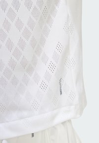Camiseta blanca con patrón de perforaciones en forma de diamante y puntos, con una textura suave y etiqueta "climacool" en el dobladillo.