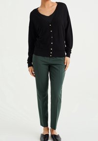 Svart kavaj med V-ringning och knäppning, matchad med gröna skräddarsydda byxor. Outfiten kompletteras av svarta lägenheter.