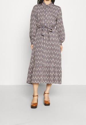 Woman wearing a patterned long-sleeve midi dress with a collar and waist tie, paired with brown ankle-strap platform heels.