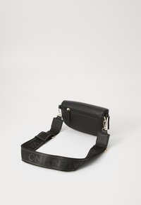 Geantă crossbody din piele neagră, cu un finisaj texturat, buzunar cu fermoar și curea detașabilă cu un logo. Accente de hardware aurie vizibile.