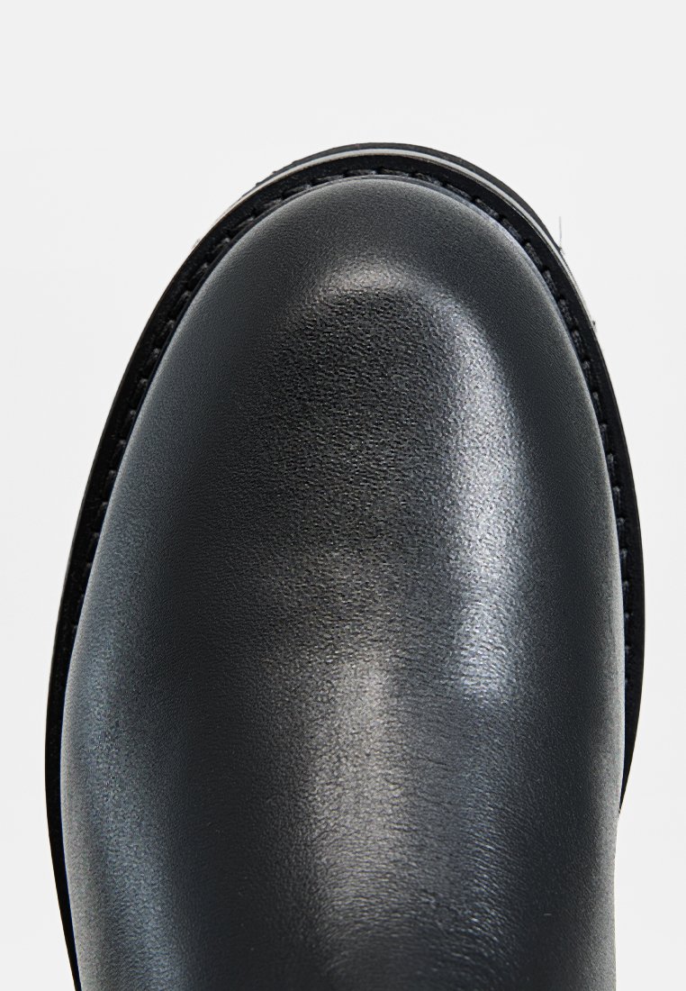 Schwarze Lederstiefel mit einer glatten, abgerundeten Zehenpartie, subtiler Textur und kontrastierender Naht entlang der Kante der Sohle.