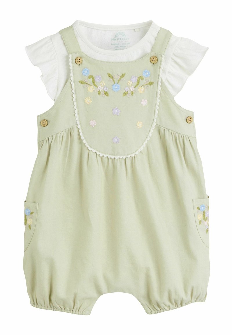 Salopette verde chiaro con design floreale ricamato, camicia bianca a balze sottostante, dettagli con bottoni e aperture delle gambe elasticizzate.