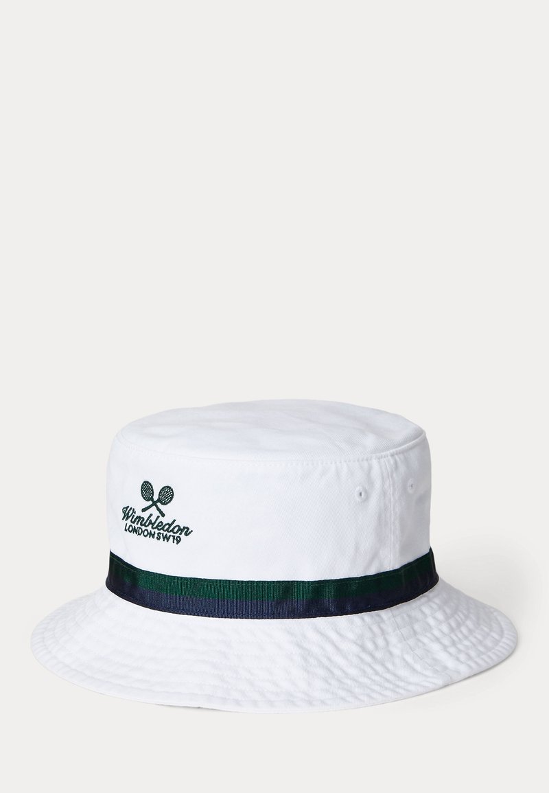 Bijela kape od pamuka s teksturiranom površinom. Ima zeleni i mornarsko plavi prugasti trak i izvezeni logo "Wimbledon".