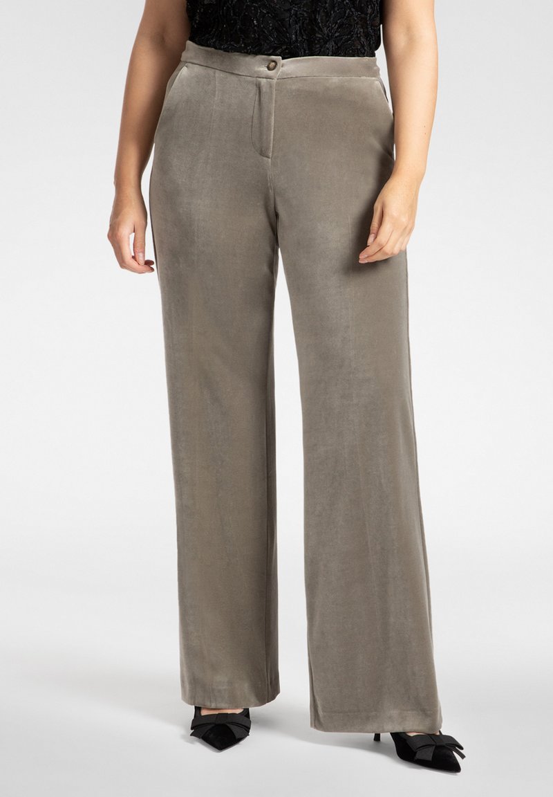 Pantaloni a gamba larga in tessuto verde tenue e morbido, con fronte piatto, chiusura con un solo bottone e texture liscia. Abbinati a scarpe nere.