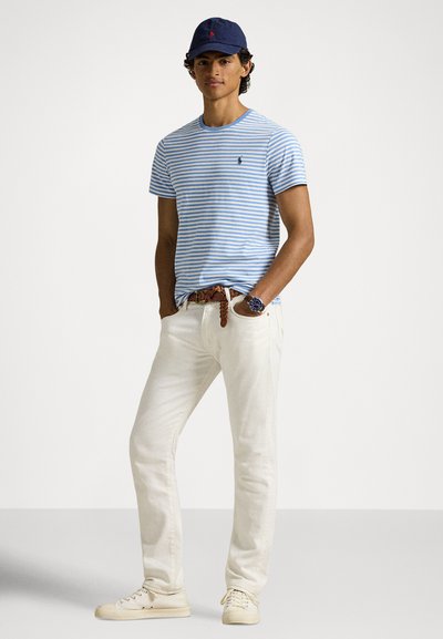 Μπλούζα με μπλε και λευκές ρίγες, σκούφο σε ναυτικό μπλε, παντελόνι ανοιχτό μπεζ, καφέ πλεκτή ζώνη, λευκά αθλητικά παπούτσια, με ρολόι στον αριστερό καρπό.