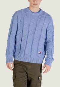 Pull bleu clair en maille avec un motif torsadé texturé, poignets et ourlet côtelés. Présente un petit patch logo de la marque sur le devant.