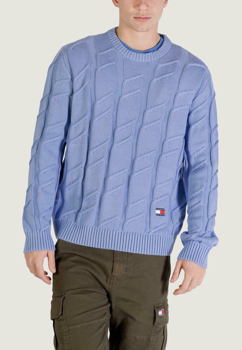 Pull bleu clair en maille avec un motif torsadé texturé, poignets et ourlet côtelés. Présente un petit patch logo de la marque sur le devant.