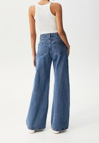Jeans de denim azul de pierna ancha con una cintura alta, que cuentan con dos bolsillos traseros y un dobladillo sin rematar. La tela tiene un acabado texturizado.