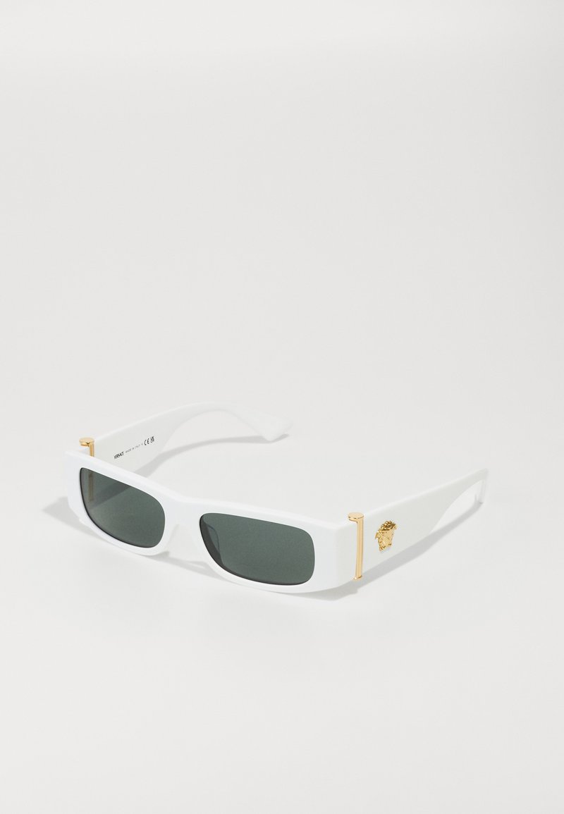 Lunettes de soleil blanches avec des verres rectangulaires, teinte vert foncé, accents dorés sur les branches et un emblème décoratif sur un côté. Texture lisse.