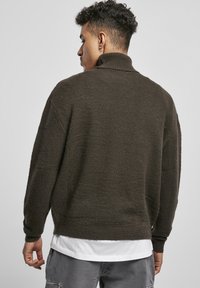 Mørkegrøn strikket sweater med høj krave, ribbede ærmer og kant. Blød tekstur og afslappet pasform. Bæres over en hvid skjorte.