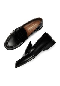 Schwarze Lederloafers mit einem erhöhten gestickten Design, glatter Oberfläche, abgerundeter Spitze, kleinem Absatz und einer dekorativen, bogenähnlichen Akzentuierung an der Vorderseite.